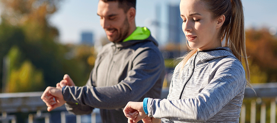 Man and woman walking outside looking at their smart watch